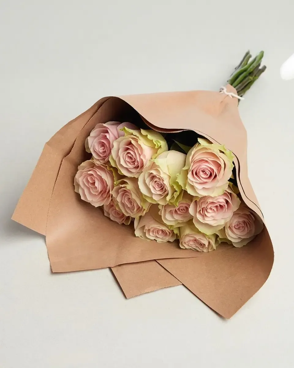 Bó hồng phấn nhạt gói giấy kraft, đặt nằm trên nền xám sáng