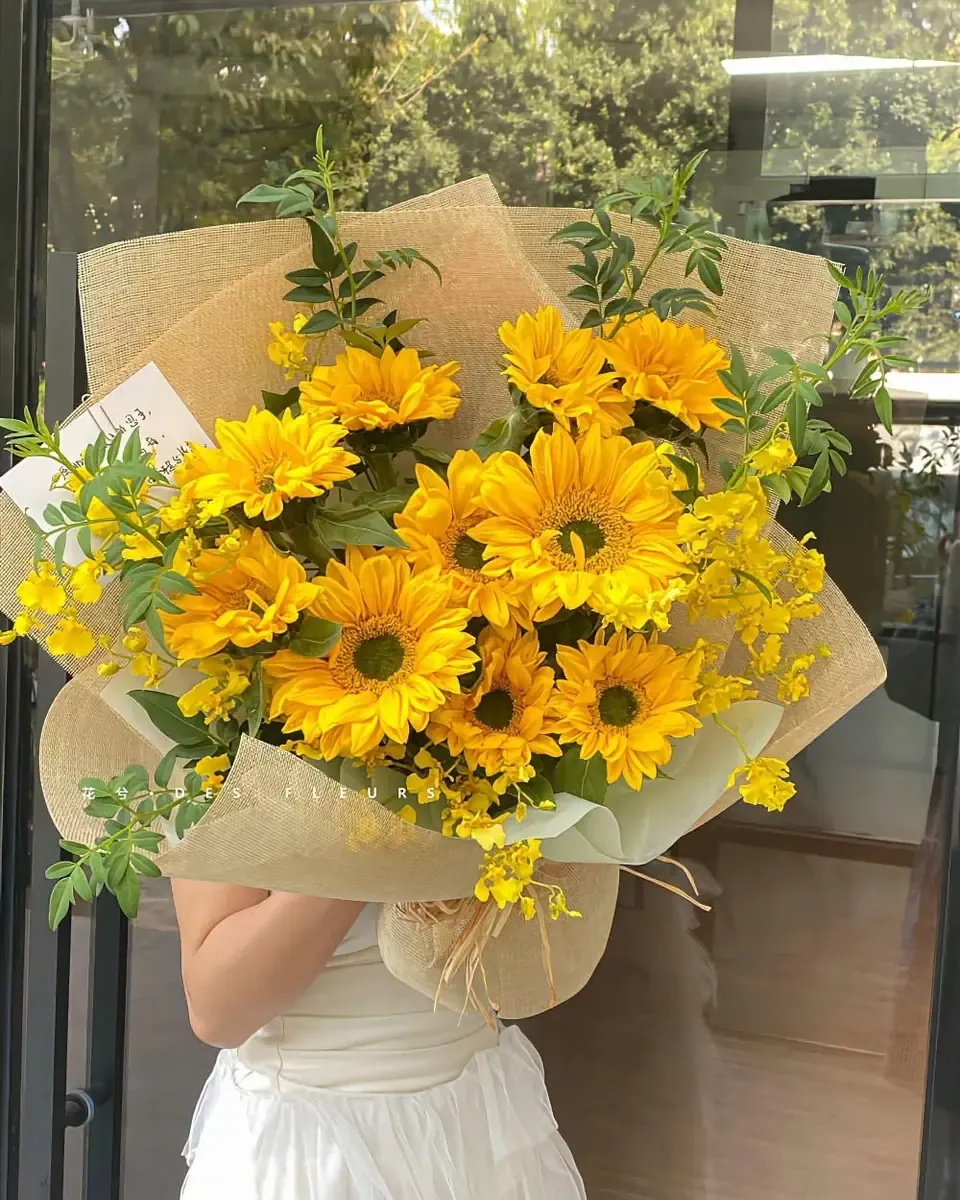 Bó hướng dương và hoa cúc vàng tươi gói giấy xanh nhạt, cô dâu váy trắng cầm che người
