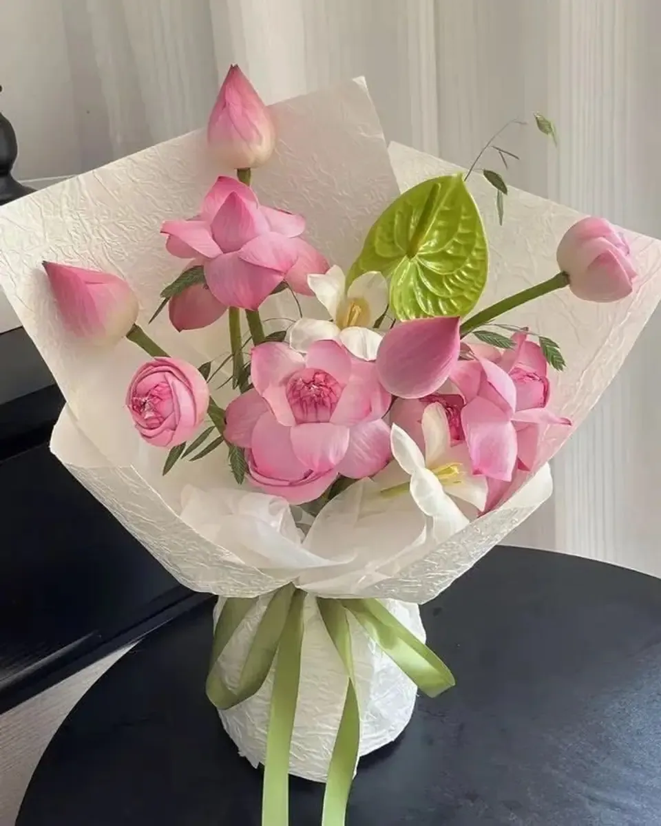 Bó sen hồng gói giấy trắng, kết hợp hoa trắng nhỏ và lá xanh, buộc ruy băng xanh lá