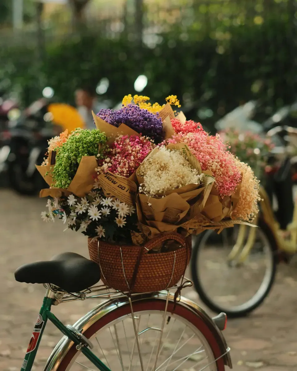 Giỏ đan trước xe đạp chất đầy hoa khô và hoa gói giấy kraft trên con đường có bóng cây