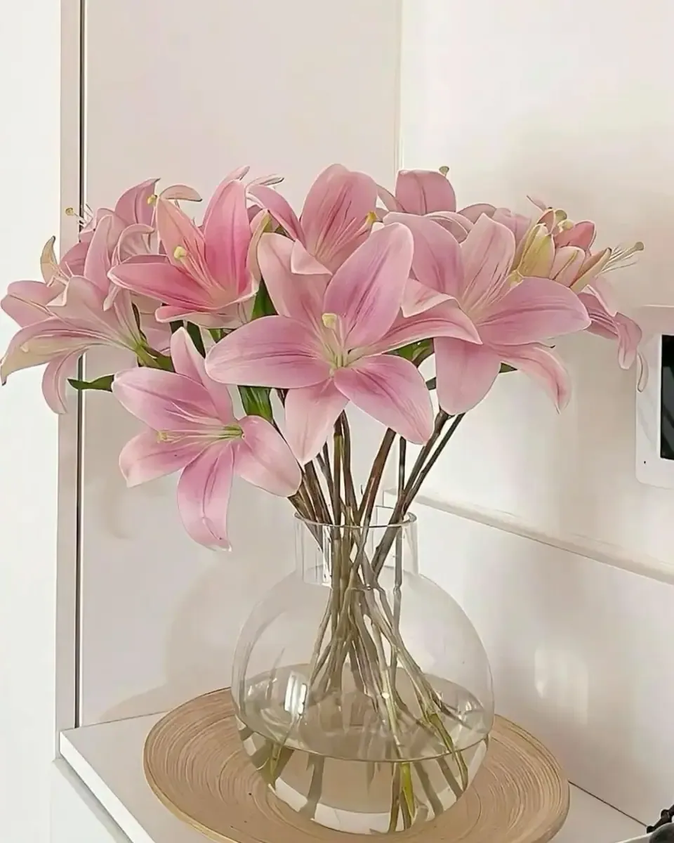 Những cành lily hồng trong bình thủy tinh tròn đặt bên khung cửa sáng