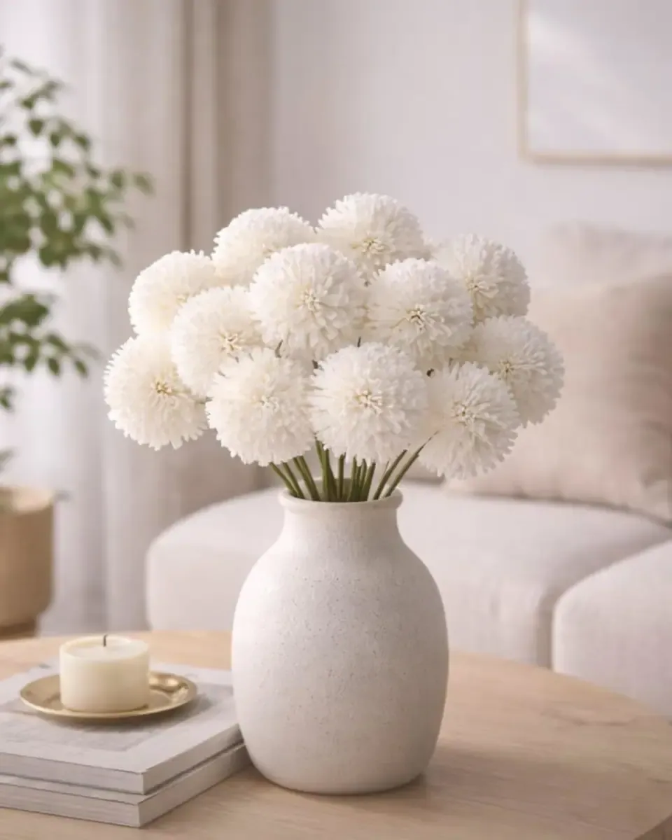 Bình gốm trắng tròn có đường gân cắm hoa cúc trắng cùng nụ nhỏ trên bàn cạnh cửa sổ
