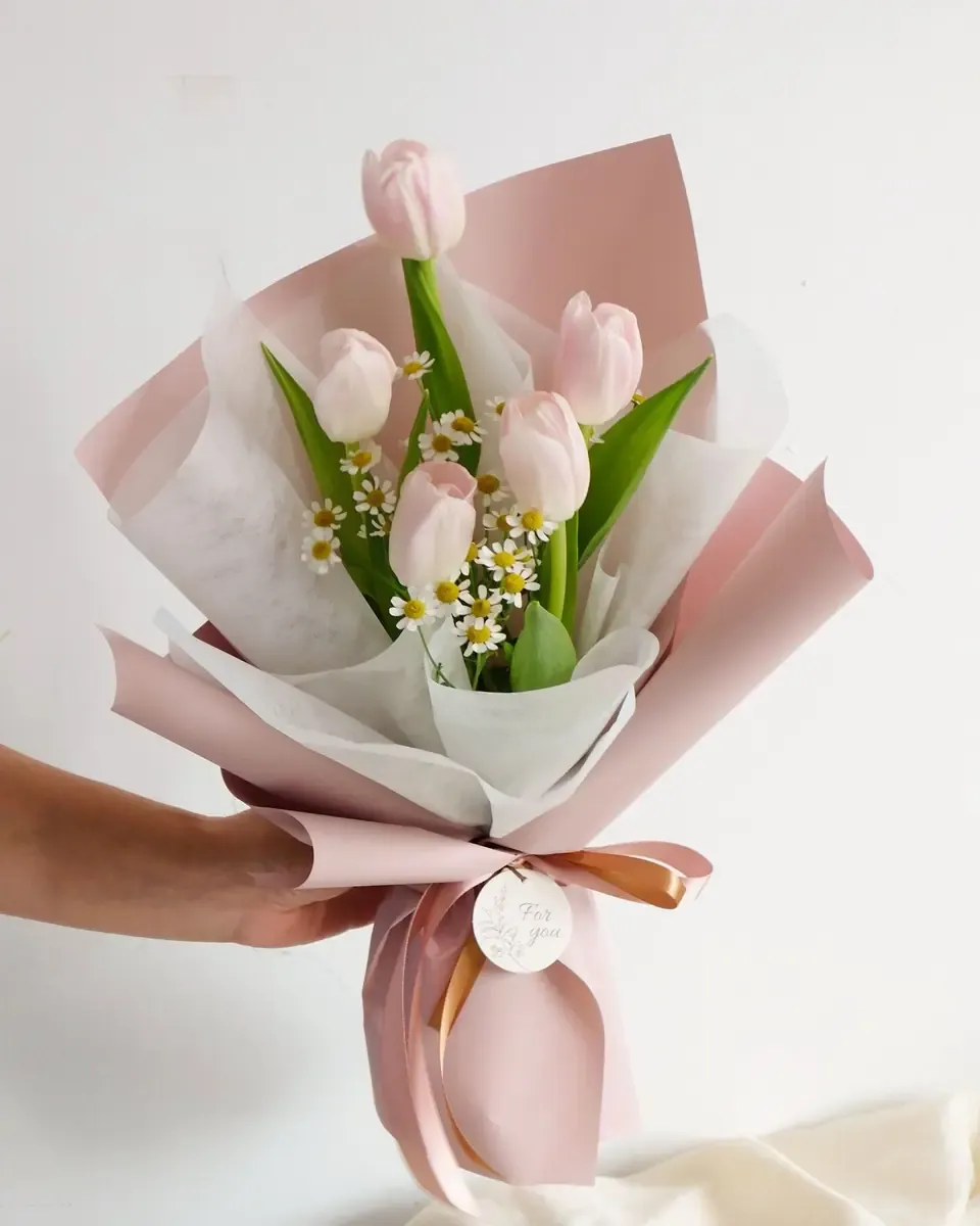 Bó tulip hồng nhạt xen hoa trắng nhỏ gói giấy hồng phấn và trắng, buộc ruy băng cam