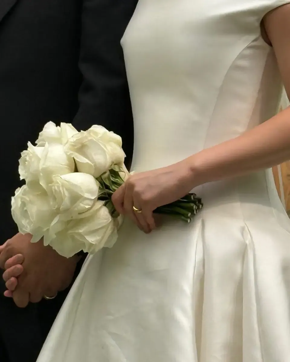 Cô dâu váy trắng nhiều lớp cầm bó hoa hồng kem và lisianthus gọn trong tay