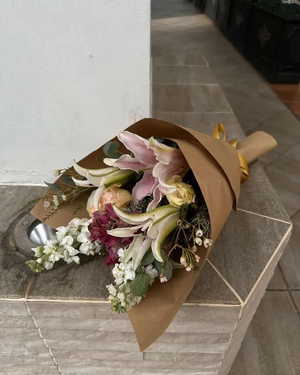 Bó hoa ly hồng gói giấy kraft đặt trên bệ đá sáng, cuống bó dây rơm