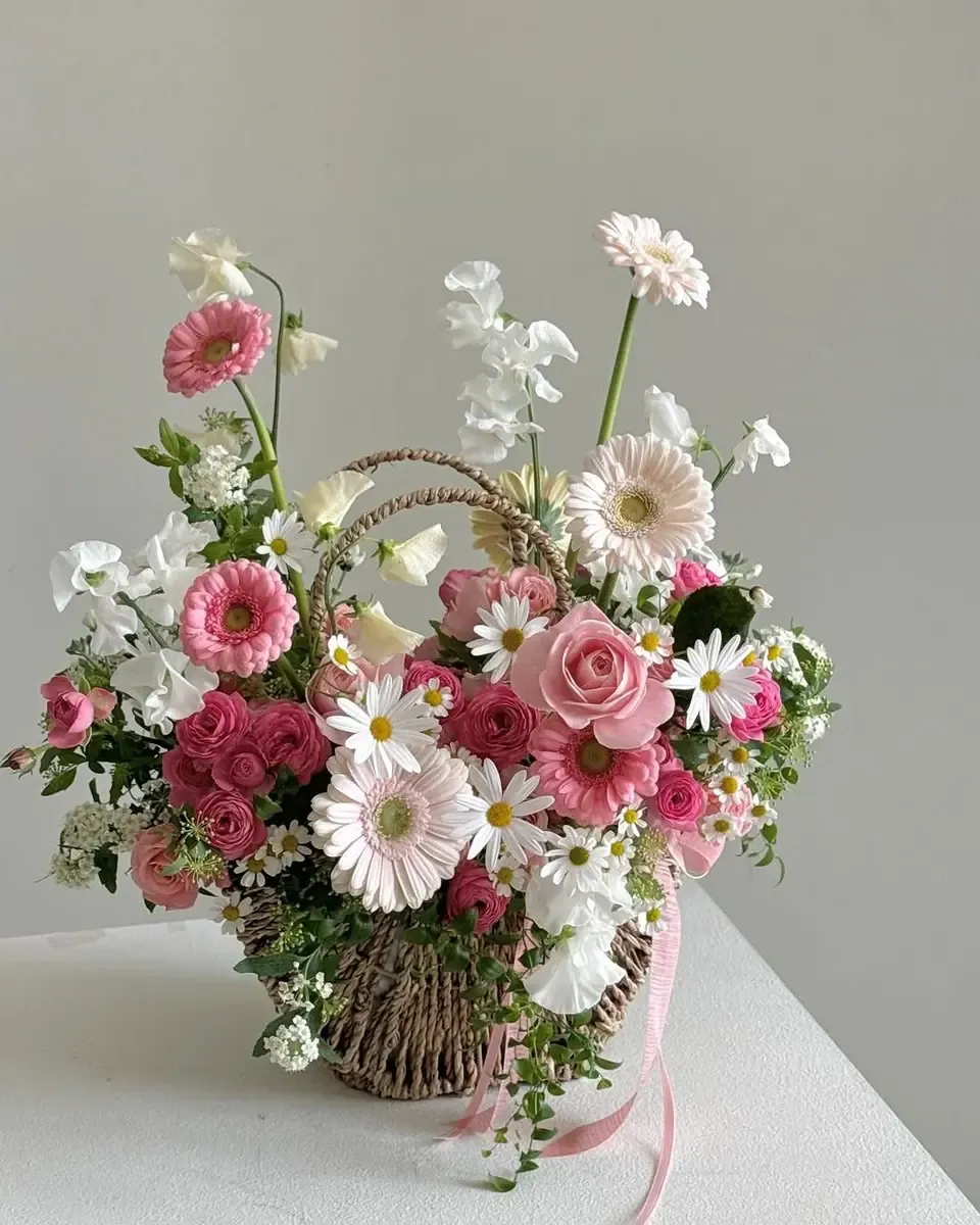 Giỏ mây cắm hoa hồng, gerbera hồng đỏ và hoa trắng trên bàn gỗ