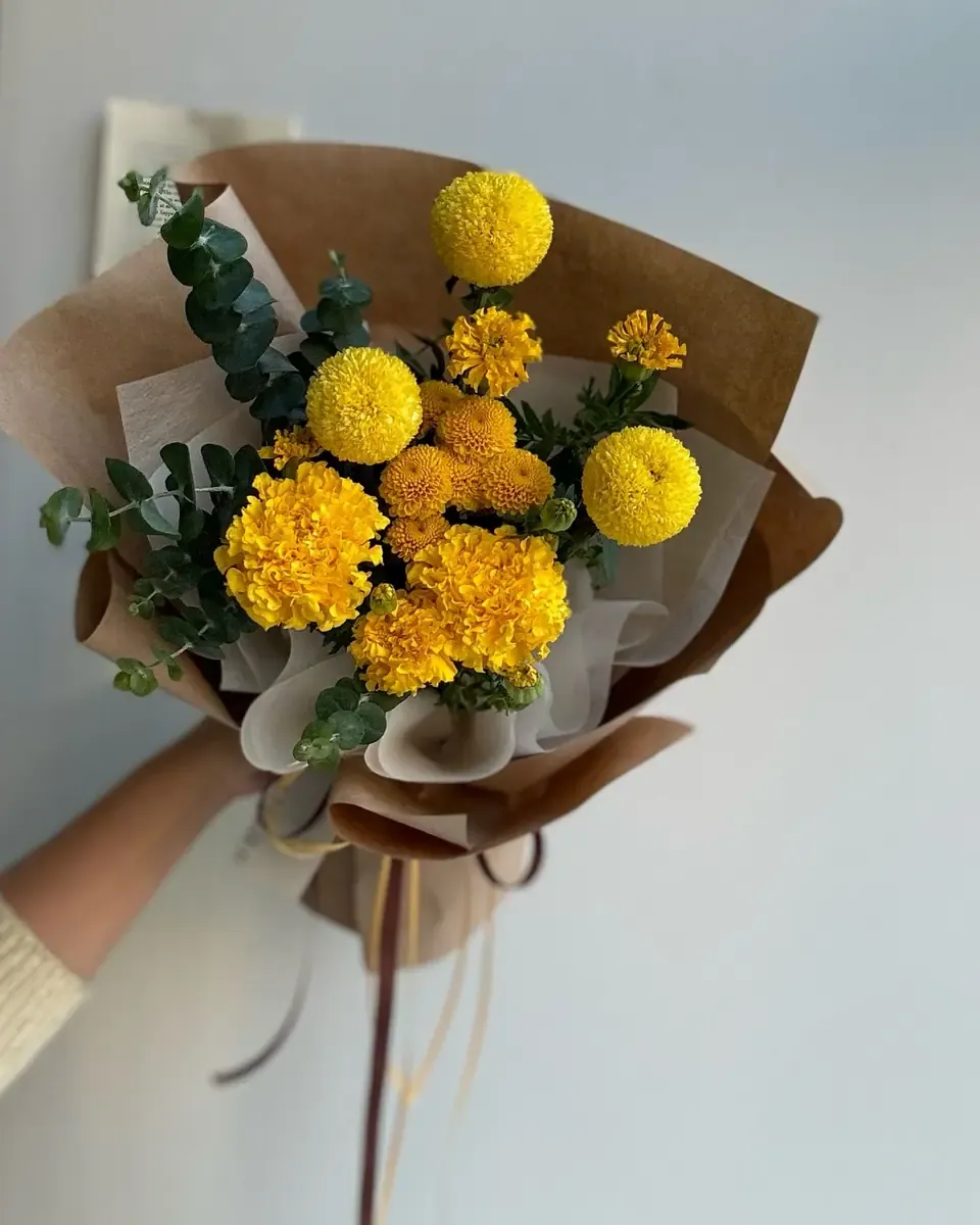 Bó hoa cúc vàng cam tròn cùng lá bạch đàn gói giấy kraft và giấy kem