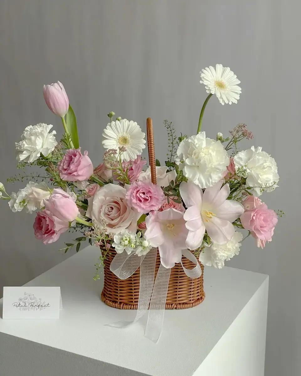 Giỏ mây cắm hoa hồng, gerbera hồng và hoa trắng đặt trên bệ trắng