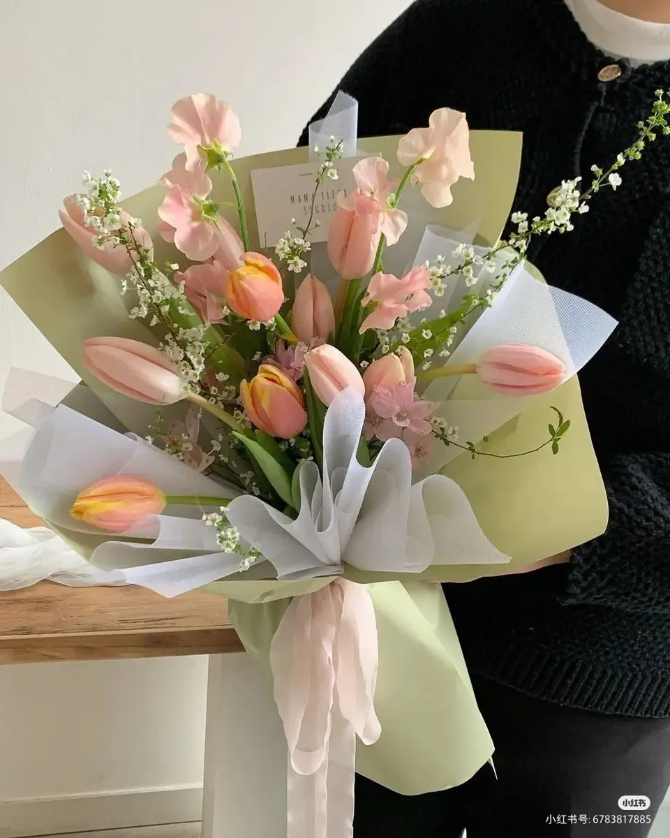 Bó tulip hồng nhạt và hoa trắng gói giấy xanh lá nhẹ buộc ruy băng