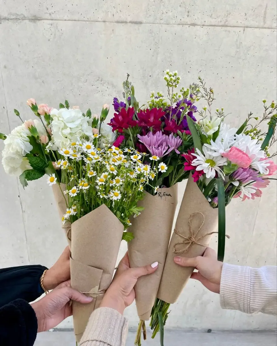 Ba bó hoa nhỏ gói giấy kraft buộc dây thừng được cầm cùng lúc trước bức tường bê tông