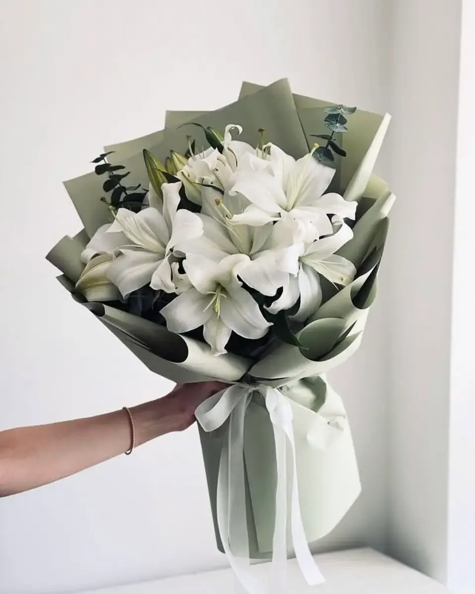Bó ly trắng gói giấy xanh sage, buộc ruy băng trắng, một tay cầm trước tường sáng