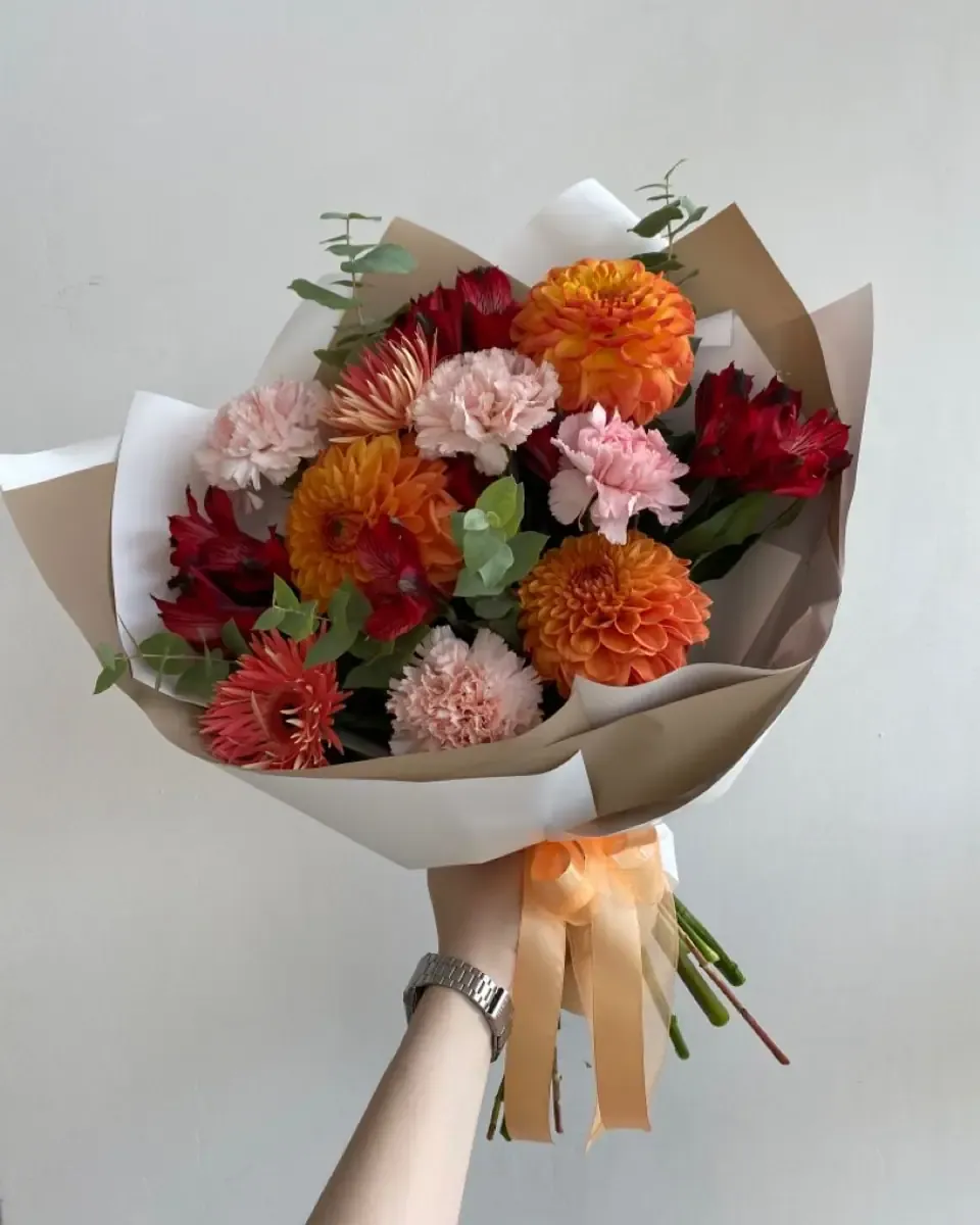 Bó hoa cam, đỏ và cẩm chướng hồng gói giấy kraft và giấy trắng, ruy băng cam