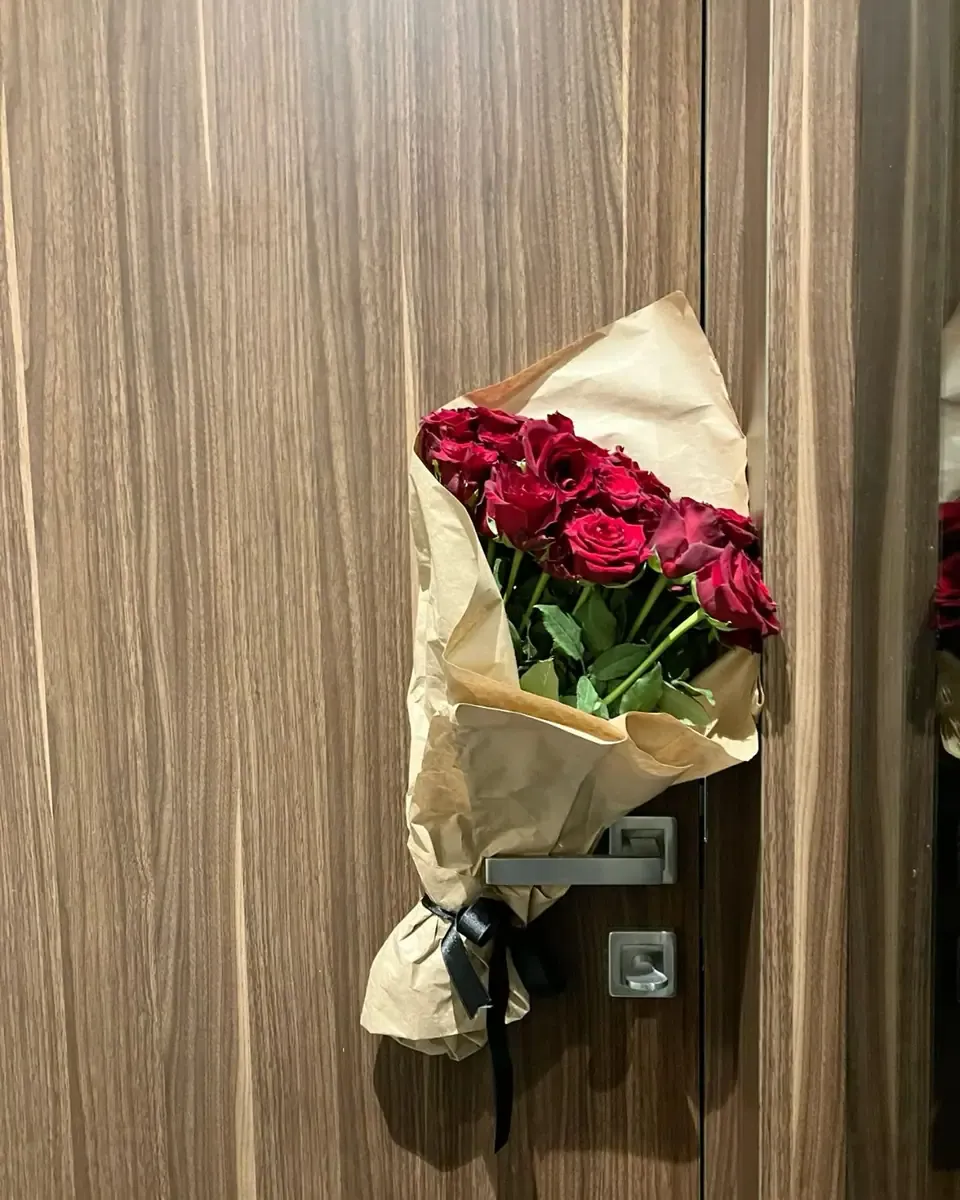 Bó hoa hồng đỏ gói giấy kraft treo trên tay nắm cửa gỗ