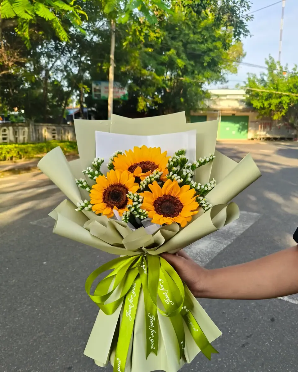 Bó hướng dương nhỏ trong giấy xanh rêu, buộc ruy băng xanh lá, được cầm trên tay