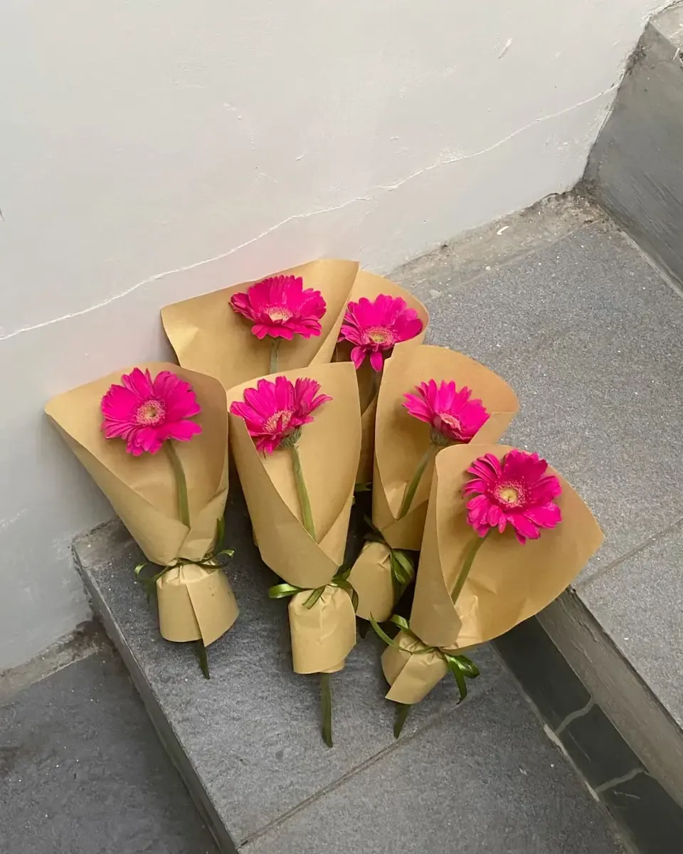 Những cành đồng tiền hồng đậm gói riêng từng cành bằng giấy kraft đặt trên bậc thềm