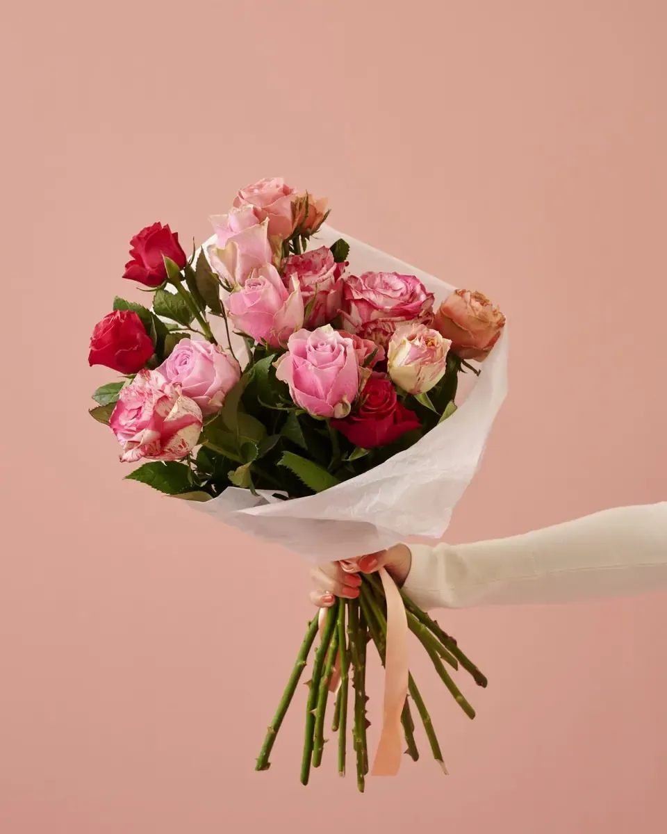 Bó hoa hồng hồng gói giấy trong suốt được cầm trên tay trước nền hồng nhạt