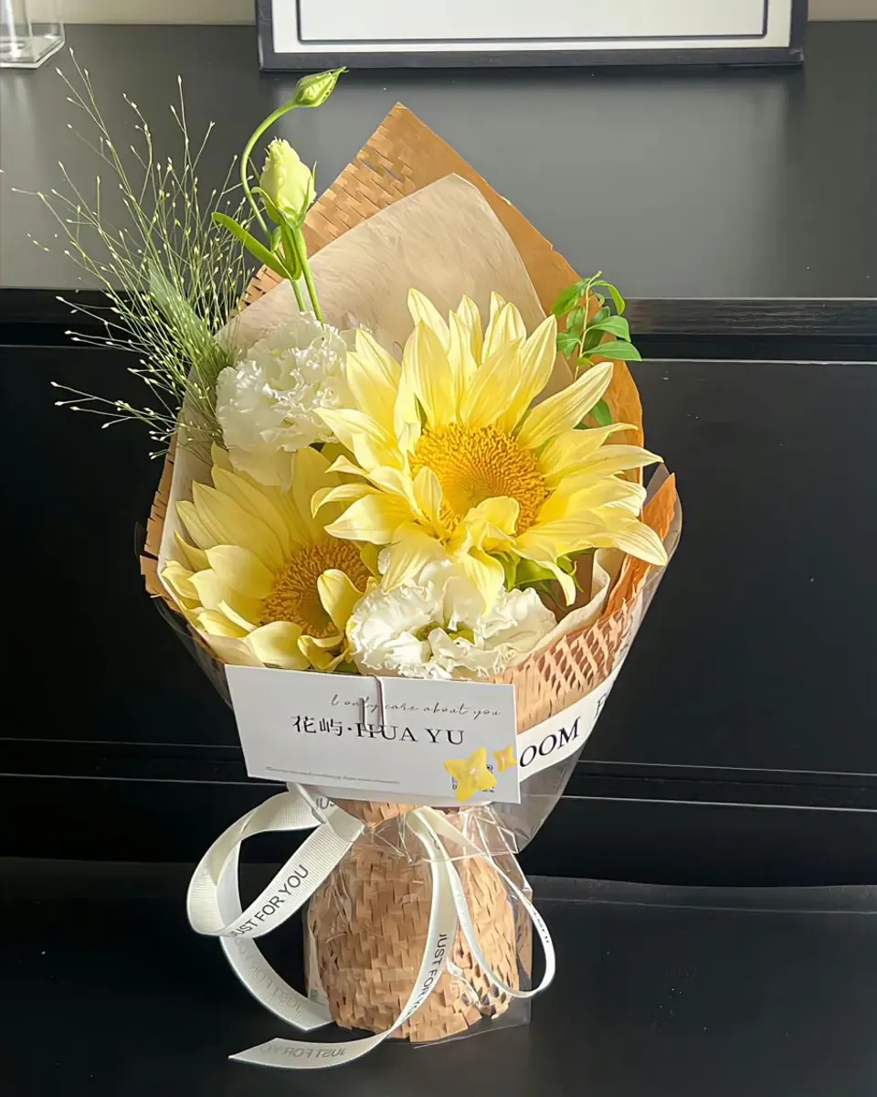 Bó hướng dương và hoa cẩm chướng trắng gói giấy kraft, đặt trên kệ tối