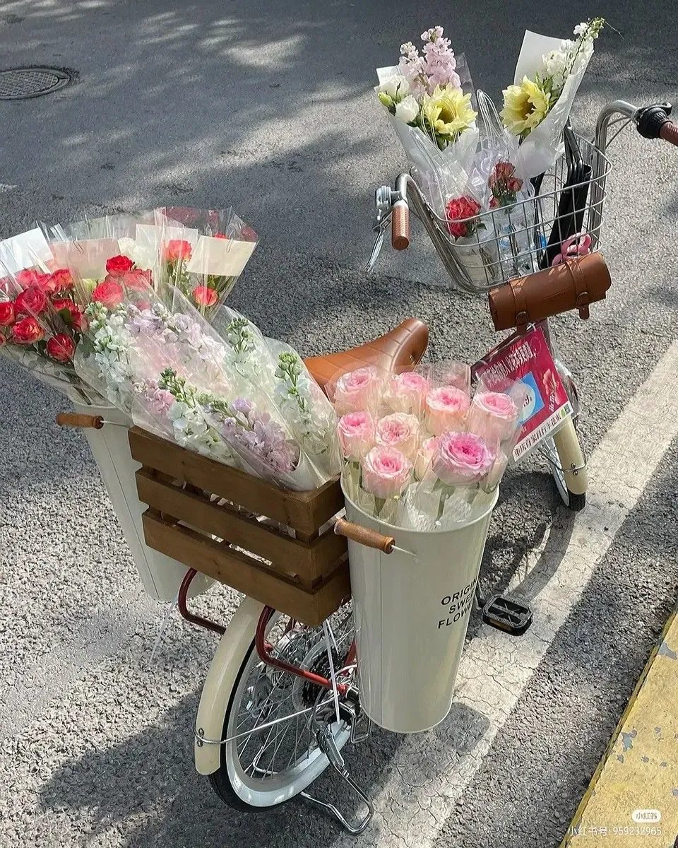 Giỏ gỗ và xô kem gắn trên xe đạp chứa hoa hồng hồng, hoa tulip gói giấy trên đường phố