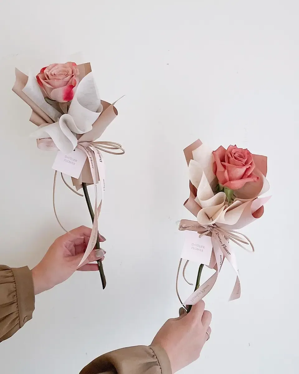 Hai bông hồng hồng đào gói giấy kem và hồng, buộc ruy băng, được hai tay cầm