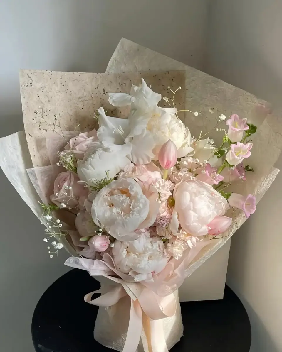Bó hoa mẫu đơn trắng, hồng nhạt và hoa nhỏ gói giấy vân đá, buộc ruy băng màu đào