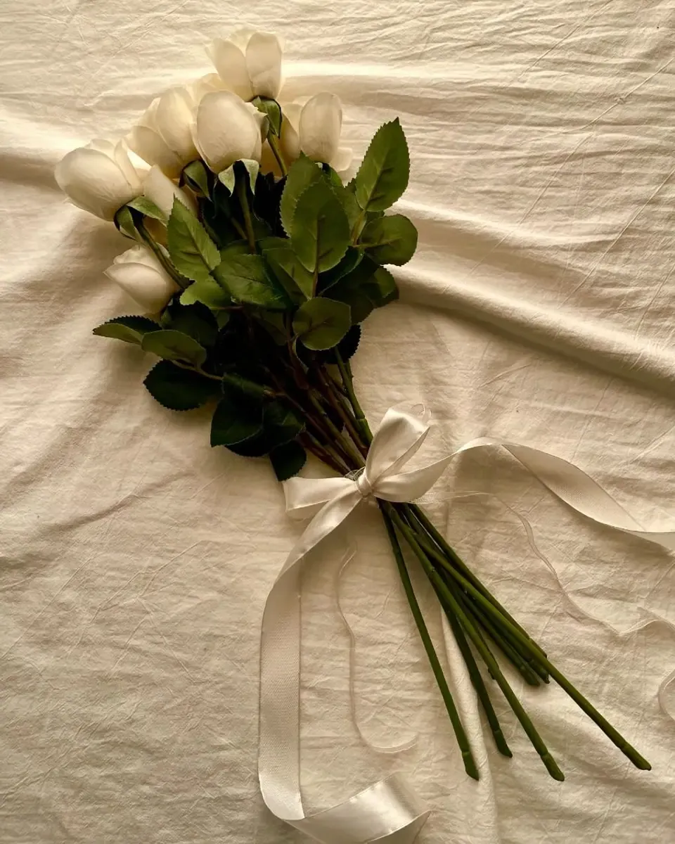 Bó tulip trắng buộc ruy băng kem đặt trên tấm vải màu kem