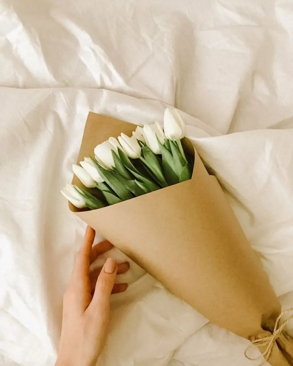 Bó tulip trắng gói giấy kraft hình nón, được cầm trên tay