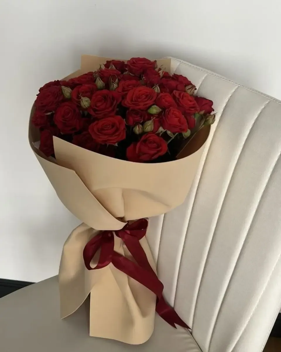 Bó hồng đỏ gói giấy be, ruy băng đỏ thẫm, đặt trên ghế