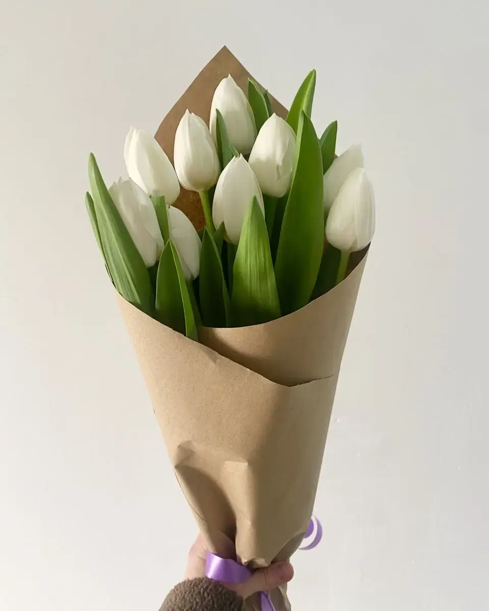 Bó tulip trắng gói giấy kraft nâu cầm trên tay trước nền tường sáng