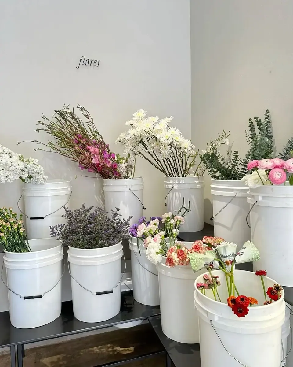 Nhiều xô trắng đựng hoa nhiều màu trong một gian hoa sáng sủa