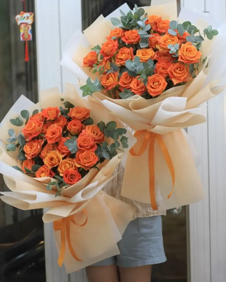 Hai bó hồng cam nhỏ gói giấy kem, buộc ruy băng cam đặt cạnh nhau