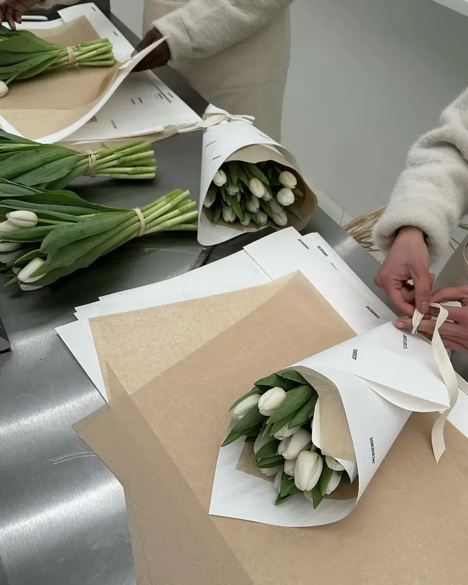 Hai bàn tay gói tulip trắng bằng giấy kraft và giấy trắng trên bàn làm việc bằng thép