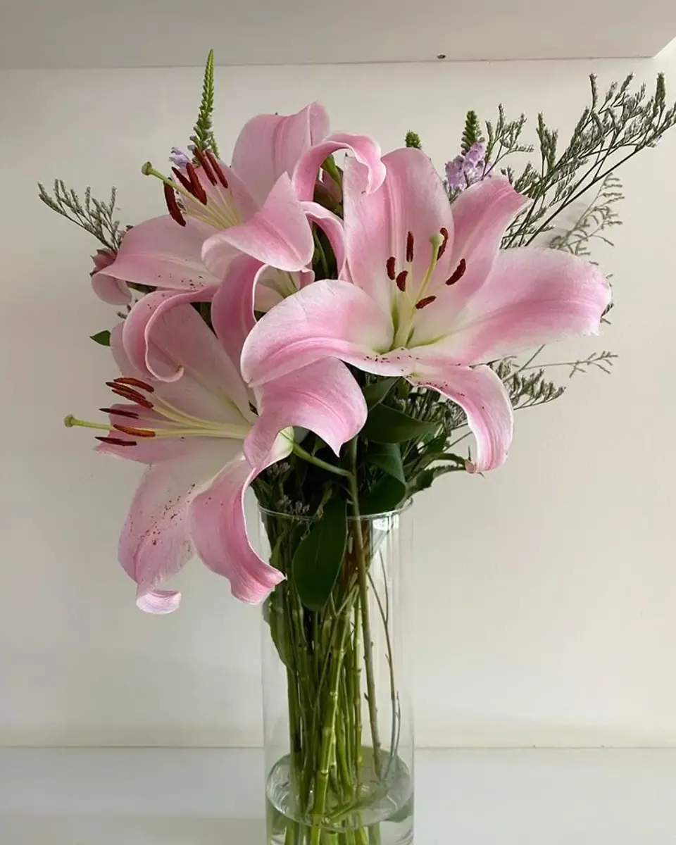 Lily hồng lớn cùng hoa khô tím nhạt trong bình thủy tinh cao trên nền tường sáng