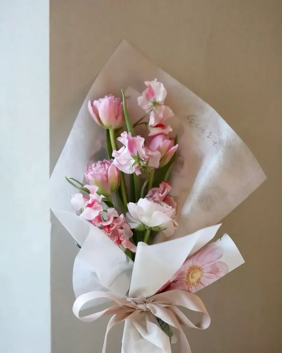 Bó tulip và hoa hồng phấn gói giấy trắng mờ, buộc ruy băng hồng nhạt