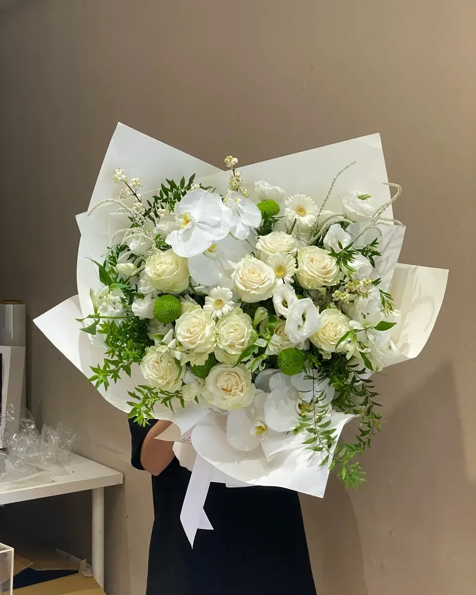 Bó hoa lan hồ điệp trắng, hồng trắng và hoa xanh nhạt gói giấy trắng, được người giữ trước ngực