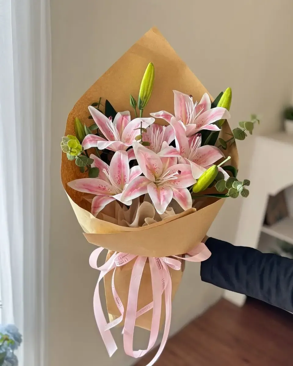 Bó hoa ly hồng nhạt gói giấy kraft hình nón, buộc nhiều dải ruy băng hồng