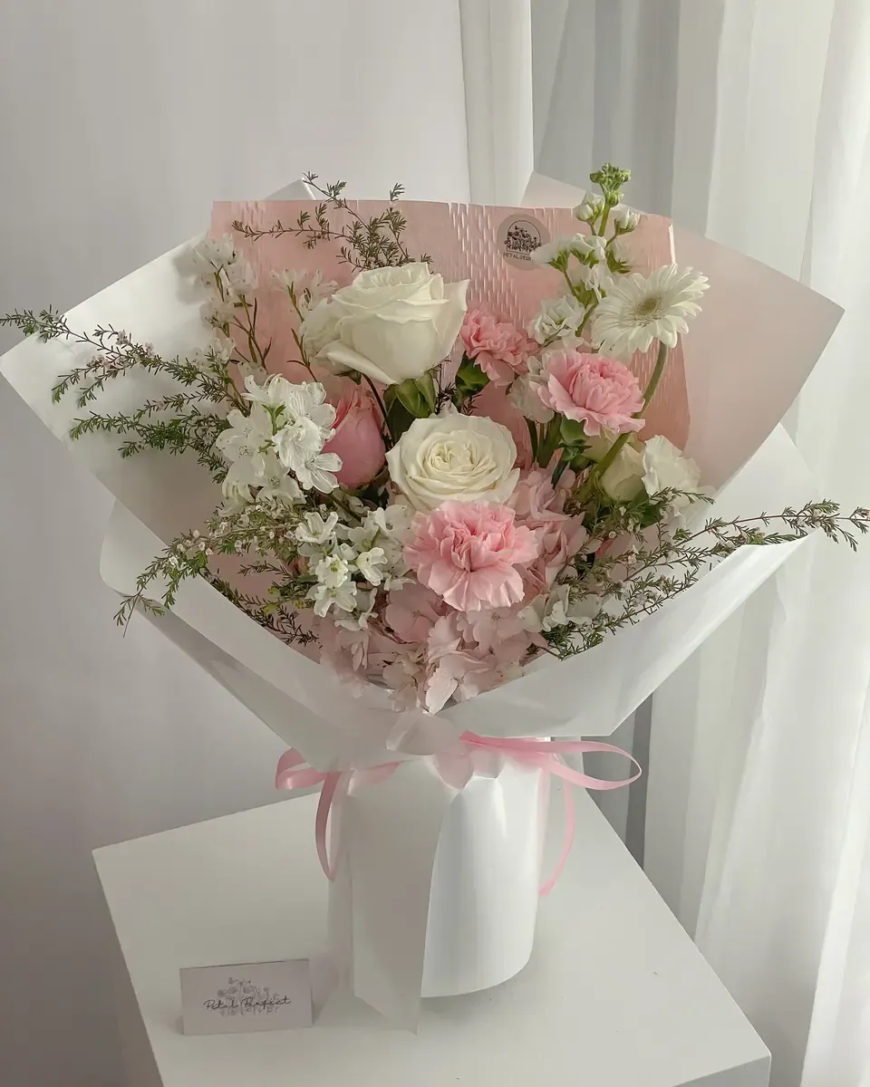 Bó hoa hồng trắng, cẩm chướng hồng và hoa nhỏ gói giấy trắng, đặt trên bục trắng