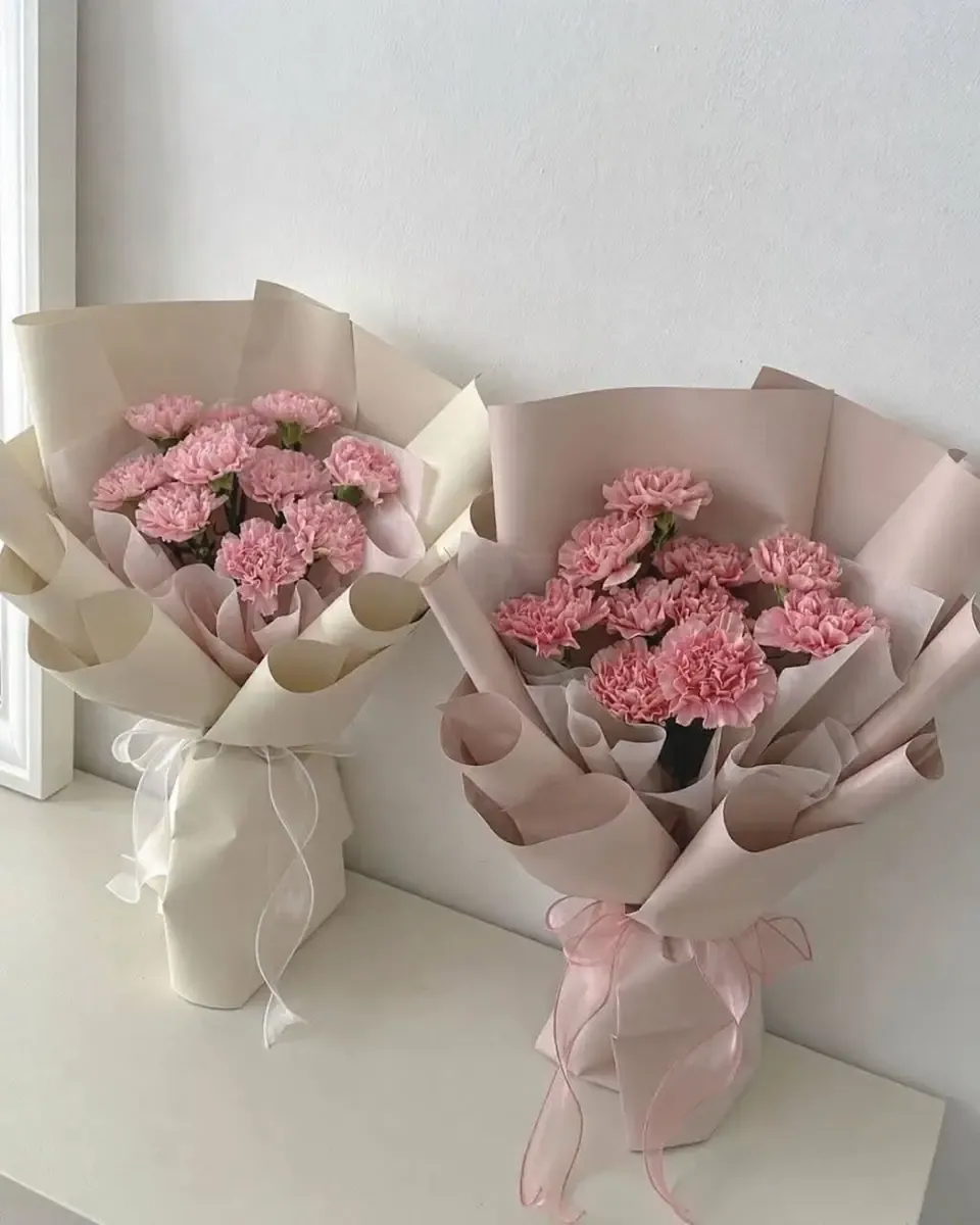 Hai bó cẩm chướng hồng gói giấy kem và hồng nhạt đặt cạnh nhau