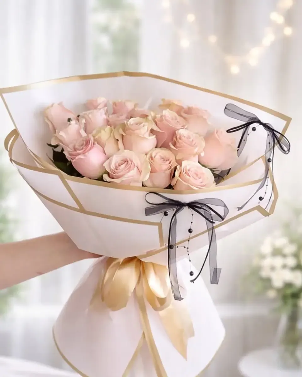 Bó hồng phấn xếp tròn trong giấy trắng viền vàng, buộc nơ đen