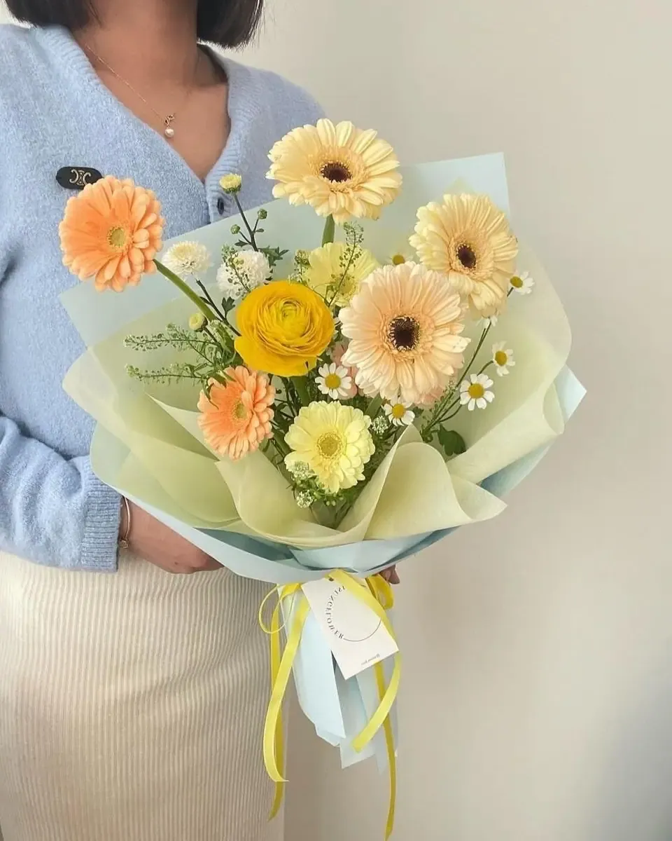 Bó gerbera cam vàng gói giấy kem buộc ruy băng vàng