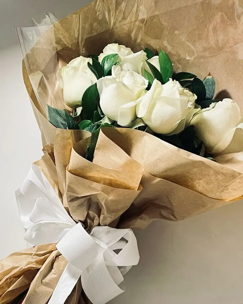 Bó hồng trắng gói giấy kraft và ruy băng trắng, lá xanh khỏe