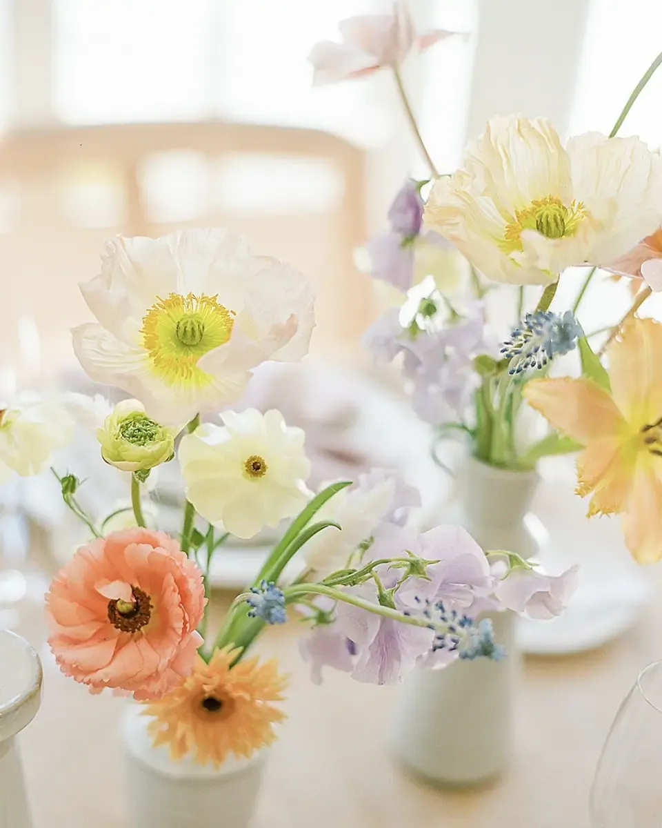 Hoa anh túc trắng, mao lương cam và gerbera cắm trong bình nhỏ trên bàn ăn