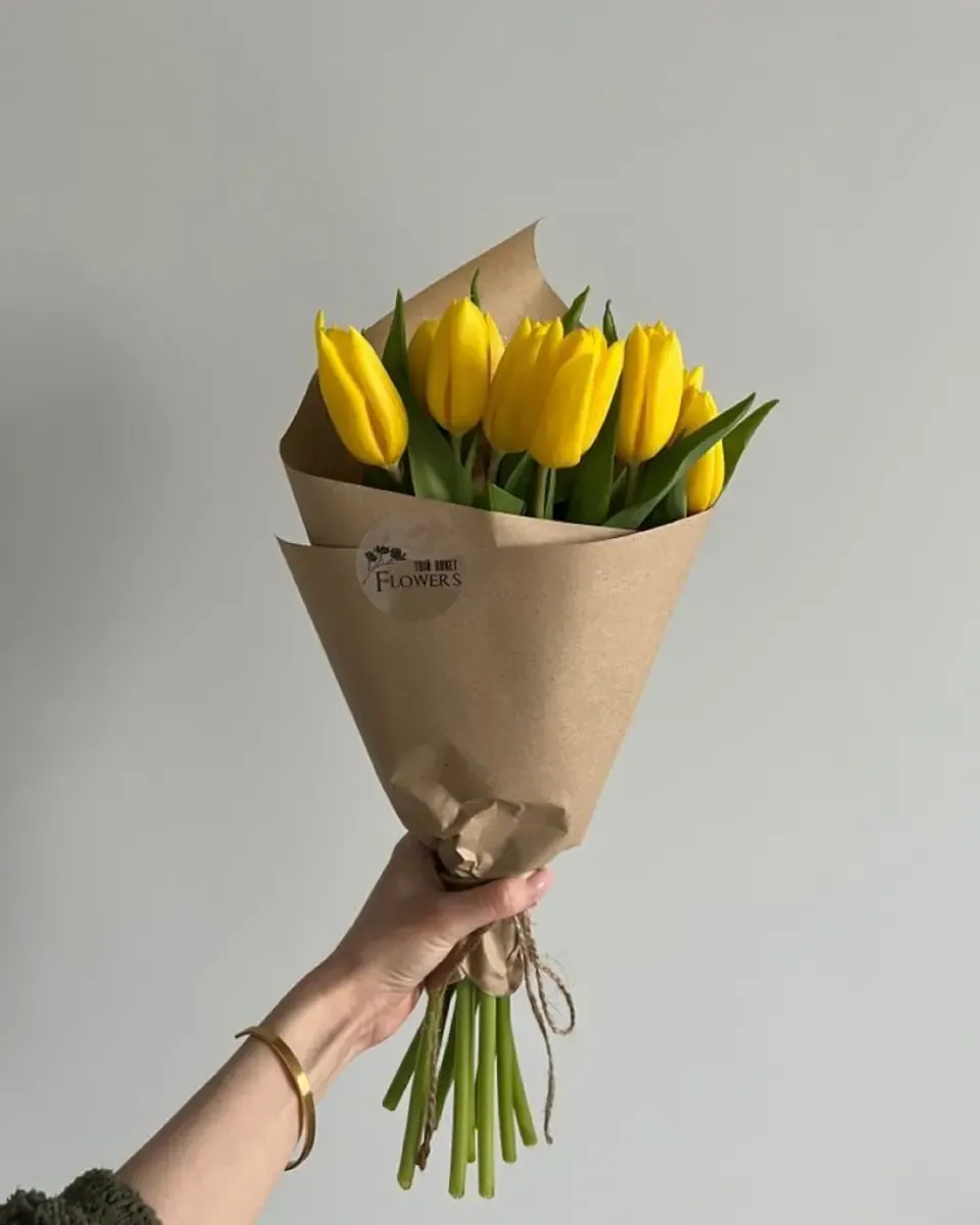 Bó tulip vàng nhỏ gói giấy kraft cầm trên tay, cuống buộc dây