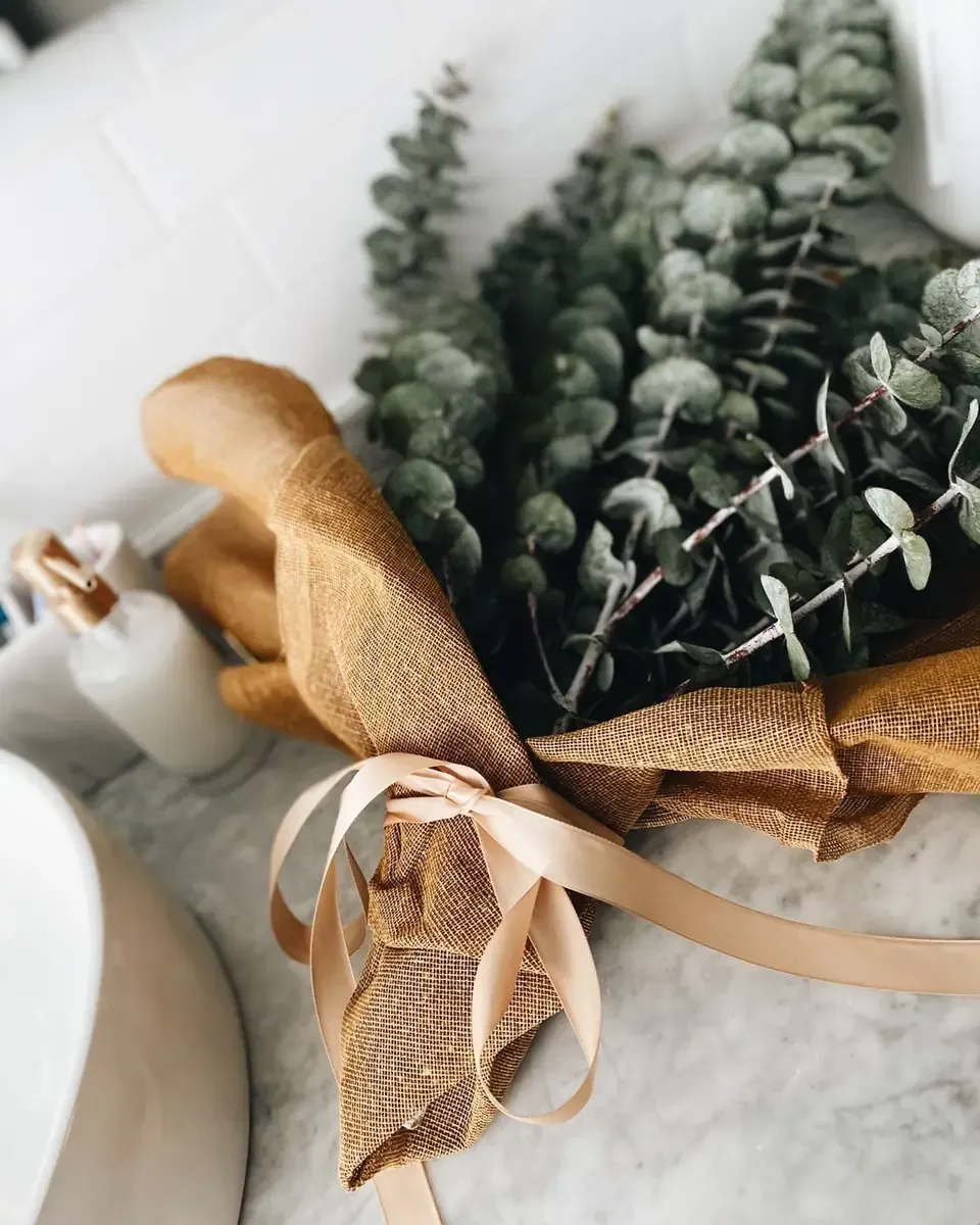 Bó lá bạch đàn xanh bạc buộc ruy băng hồng phấn và giấy bao nâu, đặt trên mặt bàn trắng