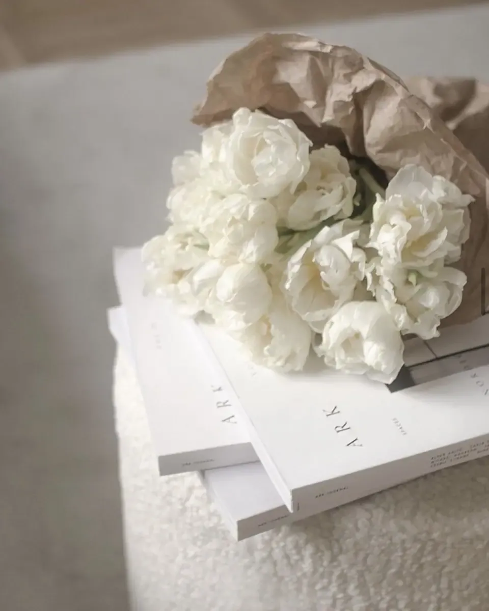 Bó mẫu đơn trắng gói giấy kraft đặt trên chồng sách