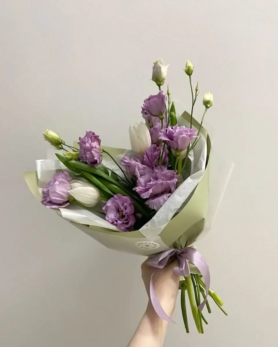 Bó lisianthus tím nhạt gói giấy kem trong tay người cầm