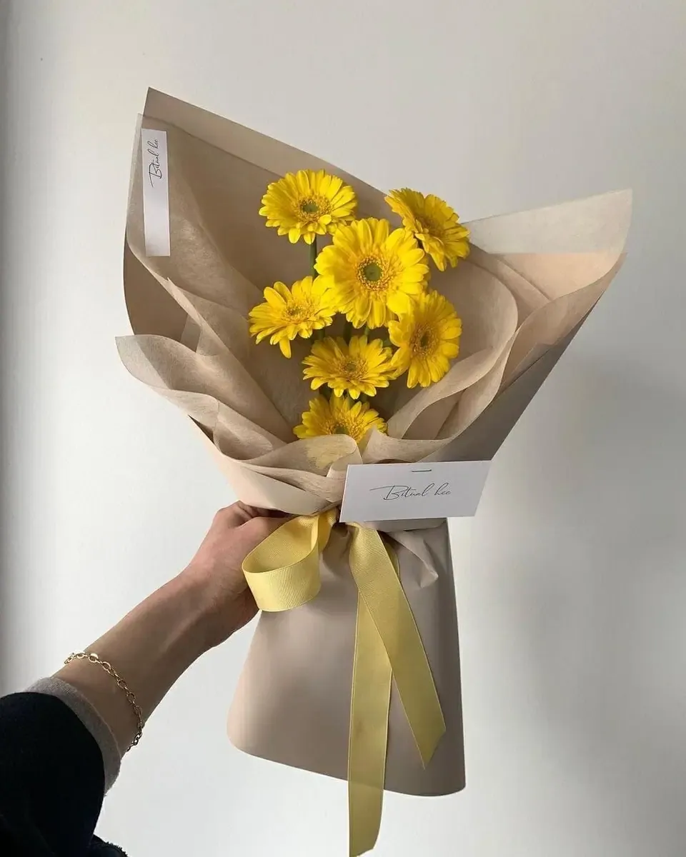 Bó hoa vàng gói giấy kraft buộc ruy băng nhạt trong tay người cầm