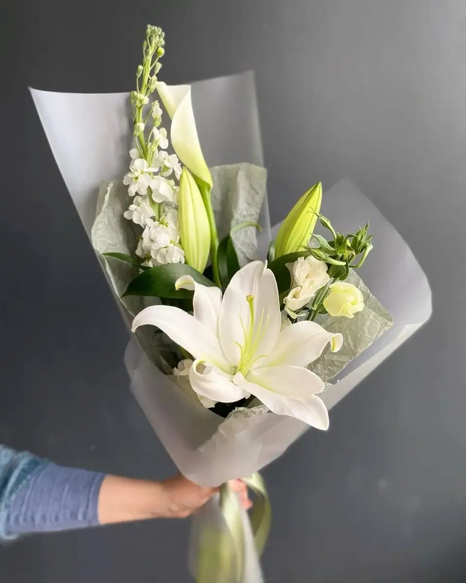 Bó ly trắng, hoa mõm sói trắng và lá xanh gói giấy xám mờ, bàn tay cầm