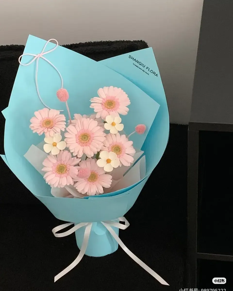 Bó hoa đồng tiền hồng và hoa nhỏ gói giấy xanh dương, buộc ruy băng trắng