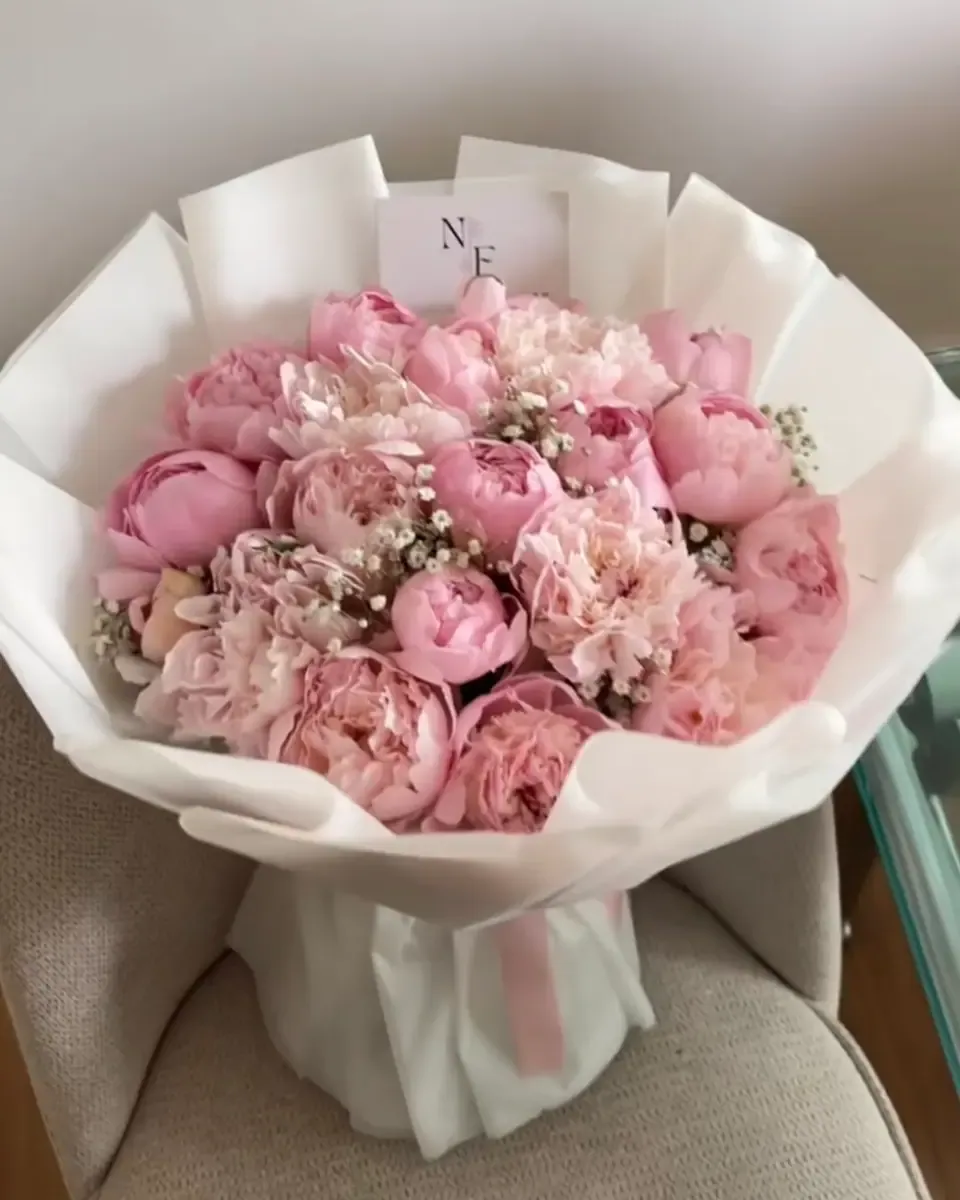 Bó mẫu đơn hồng phối hoa nhỏ gói giấy trắng nhiều lớp đặt trên ghế