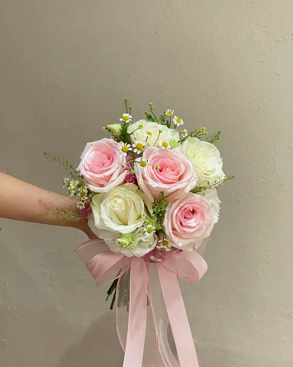 Bó hoa hồng hồng và hồng trắng xen cúc họa mi buộc ruy băng hồng trong tay cô gái
